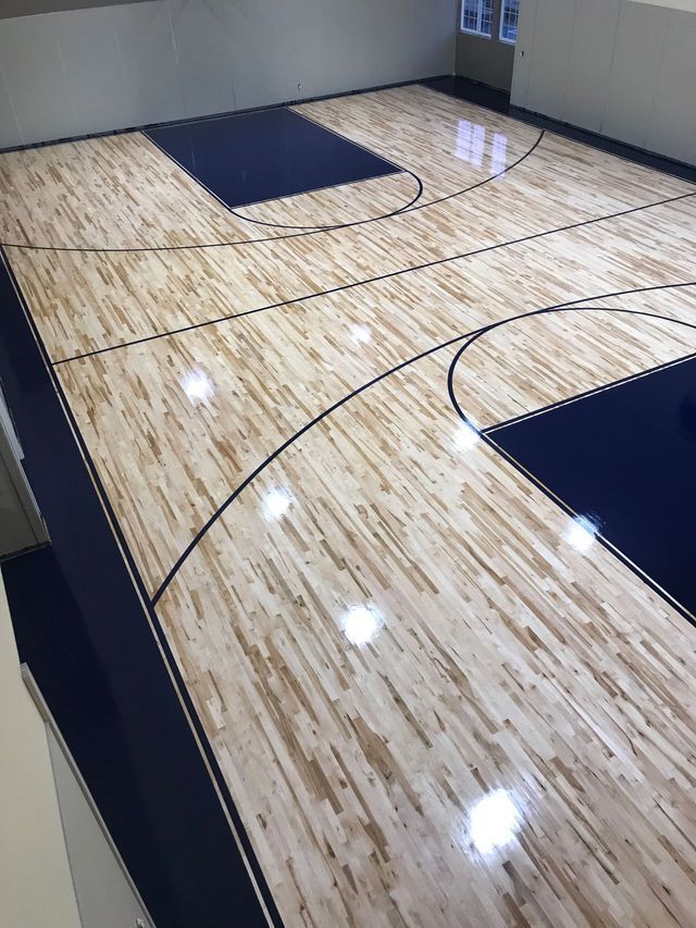 High-angle view of a basketball court with a polished hardwood floor, dark blue key areas, and black painted court lines.