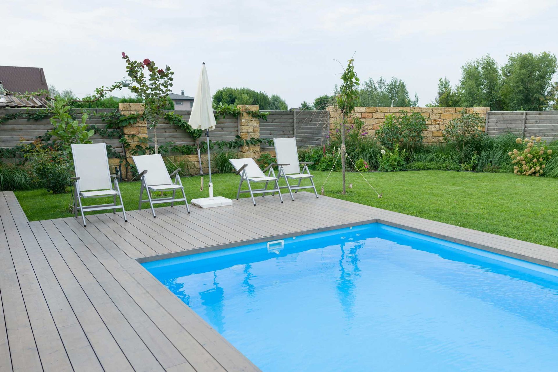 There is a swimming pool in the backyard with chairs and umbrellas.