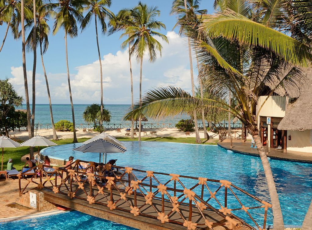 A large swimming pool with a bridge over it and palm trees in the background.
