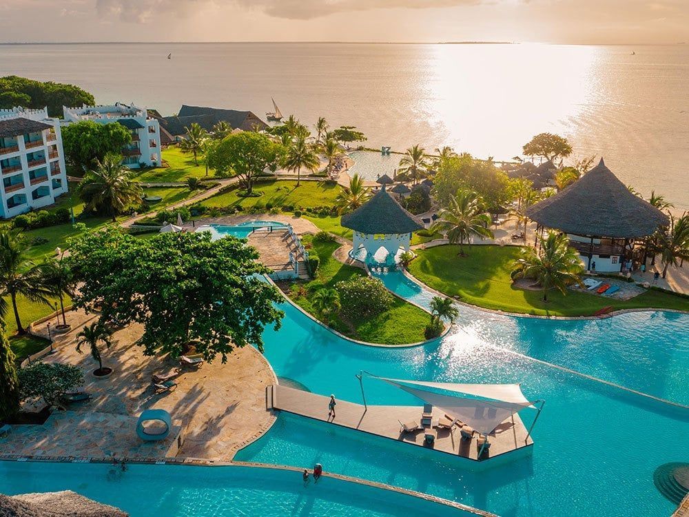An aerial view of a tropical resort with a large swimming pool surrounded by palm trees.