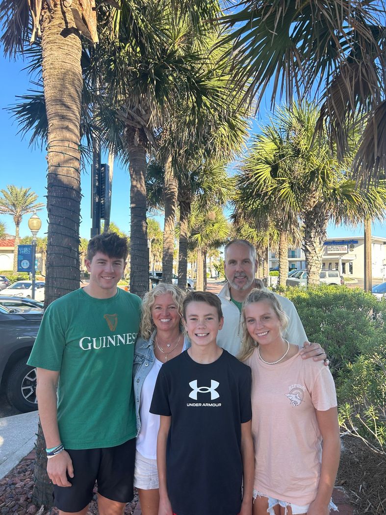 Four people standing outdoors under palm trees on a sunny day, smiling at the camera.