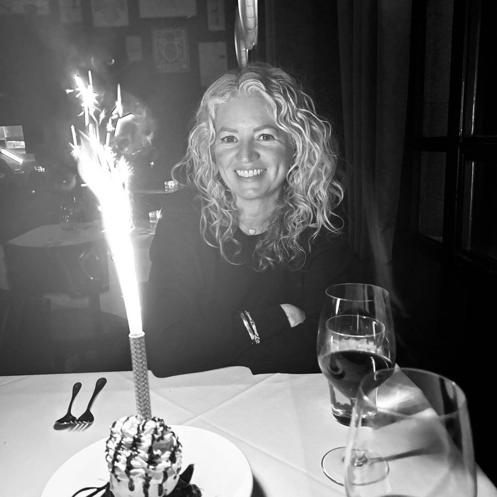 Woman smiling at a candlelit restaurant table with dessert, wine glass, and a sparkler candle