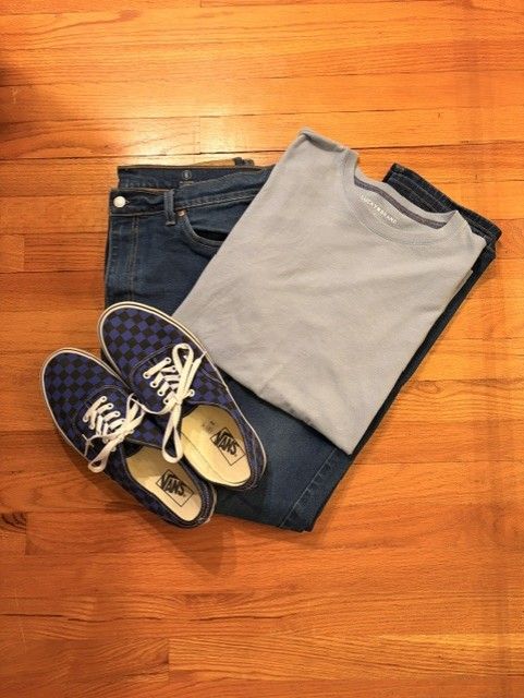 Folded jeans, gray T-shirt, and blue sneakers arranged on a wooden floor.