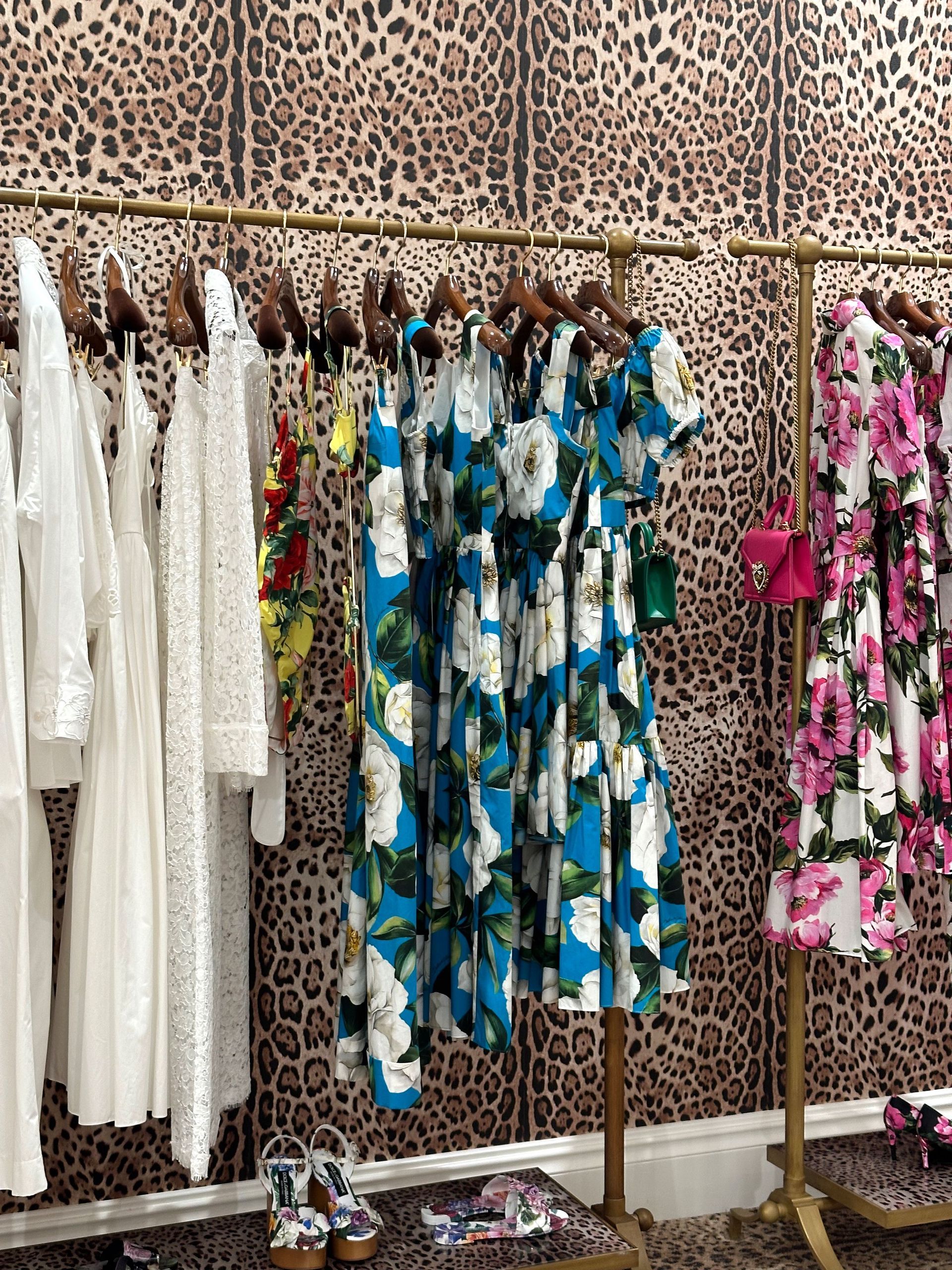 Racks of white, blue, and pink floral dresses in a clothing store against a leopard-print wall