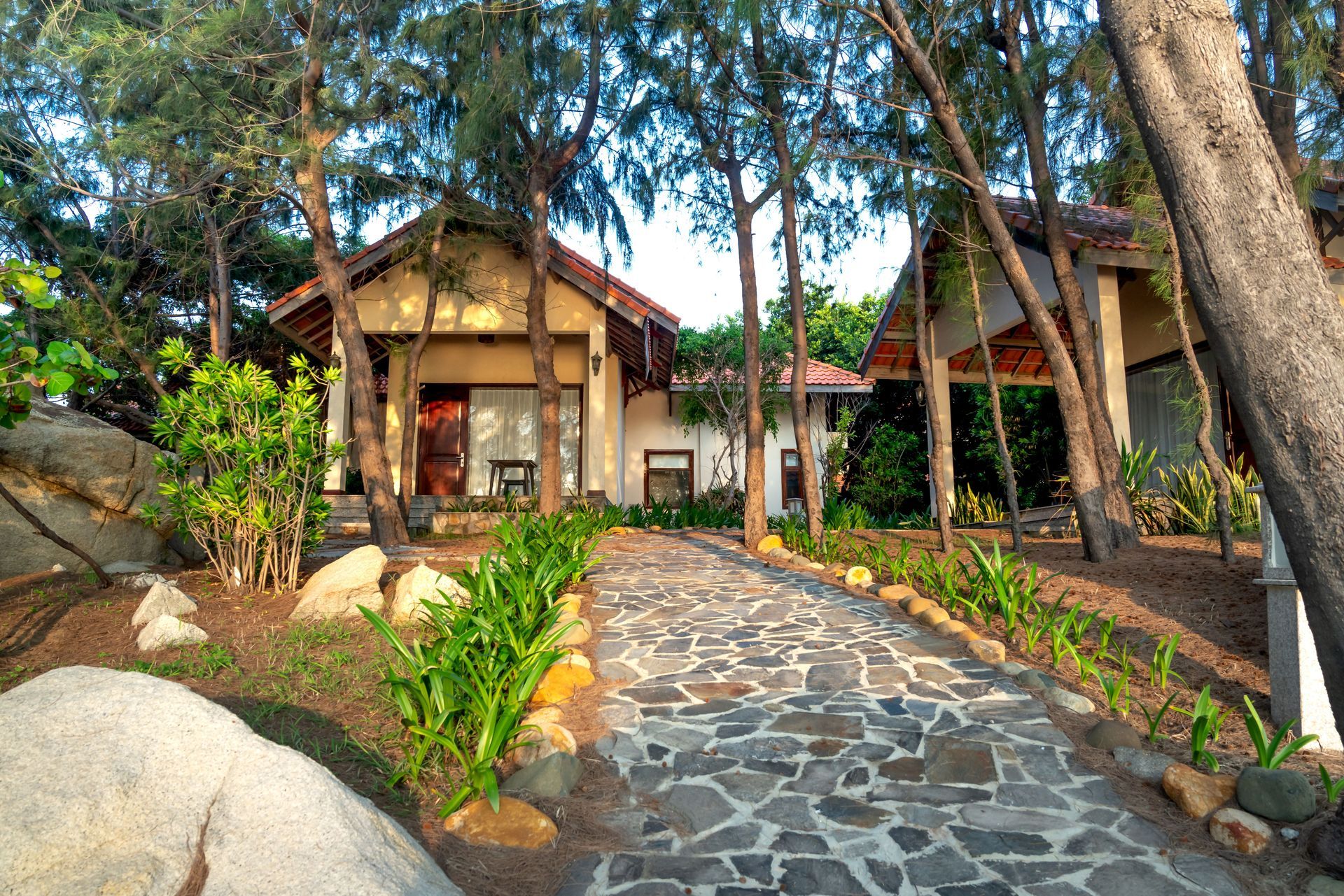 Stone path to a tropical villa with palm trees and a red-tiled roof