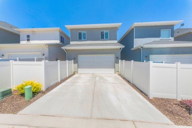 Modern two-story house with a garage and white fenced driveway under a bright blue sky