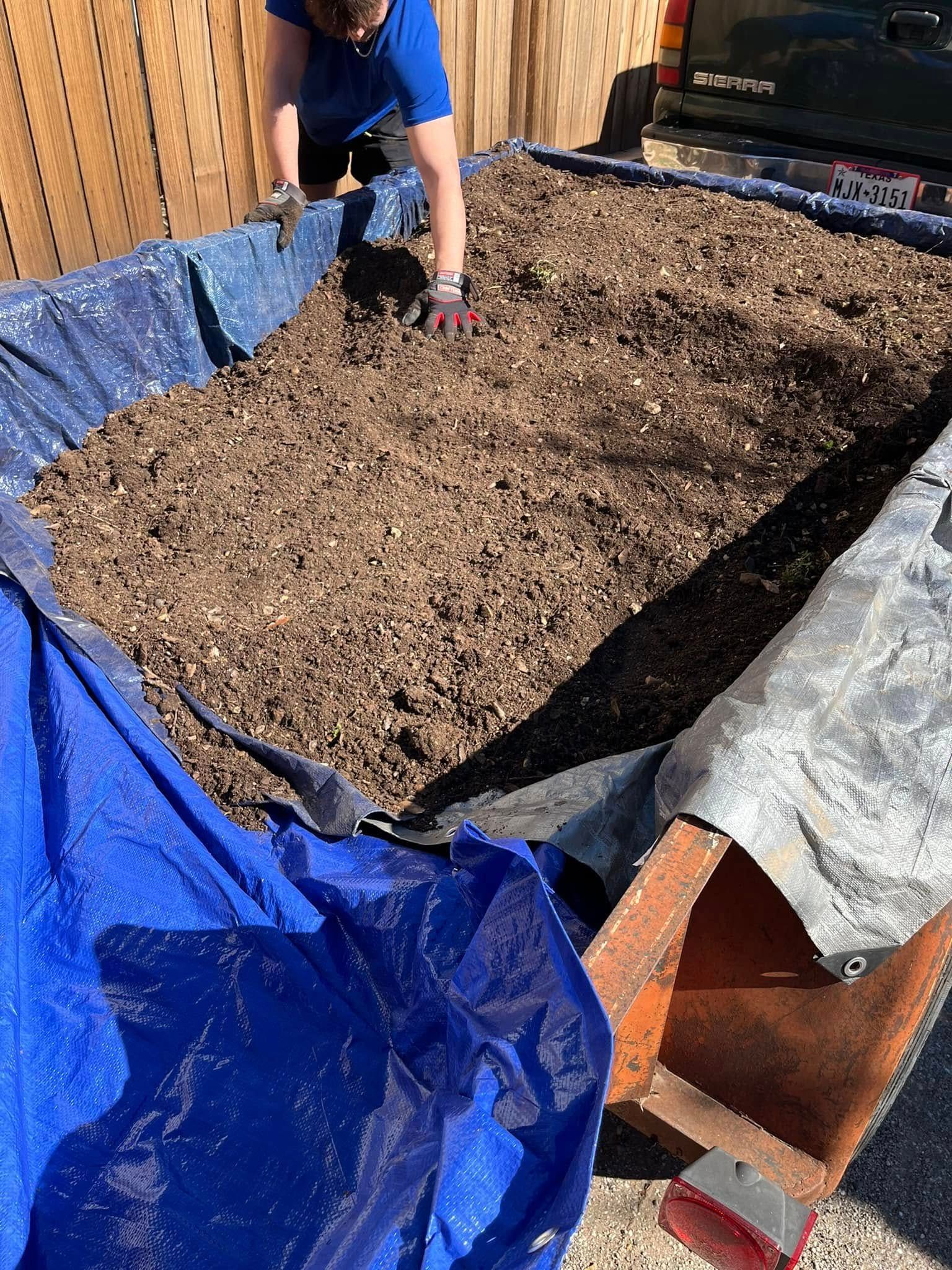 A person is standing in a pile of dirt next to a blue tarp.