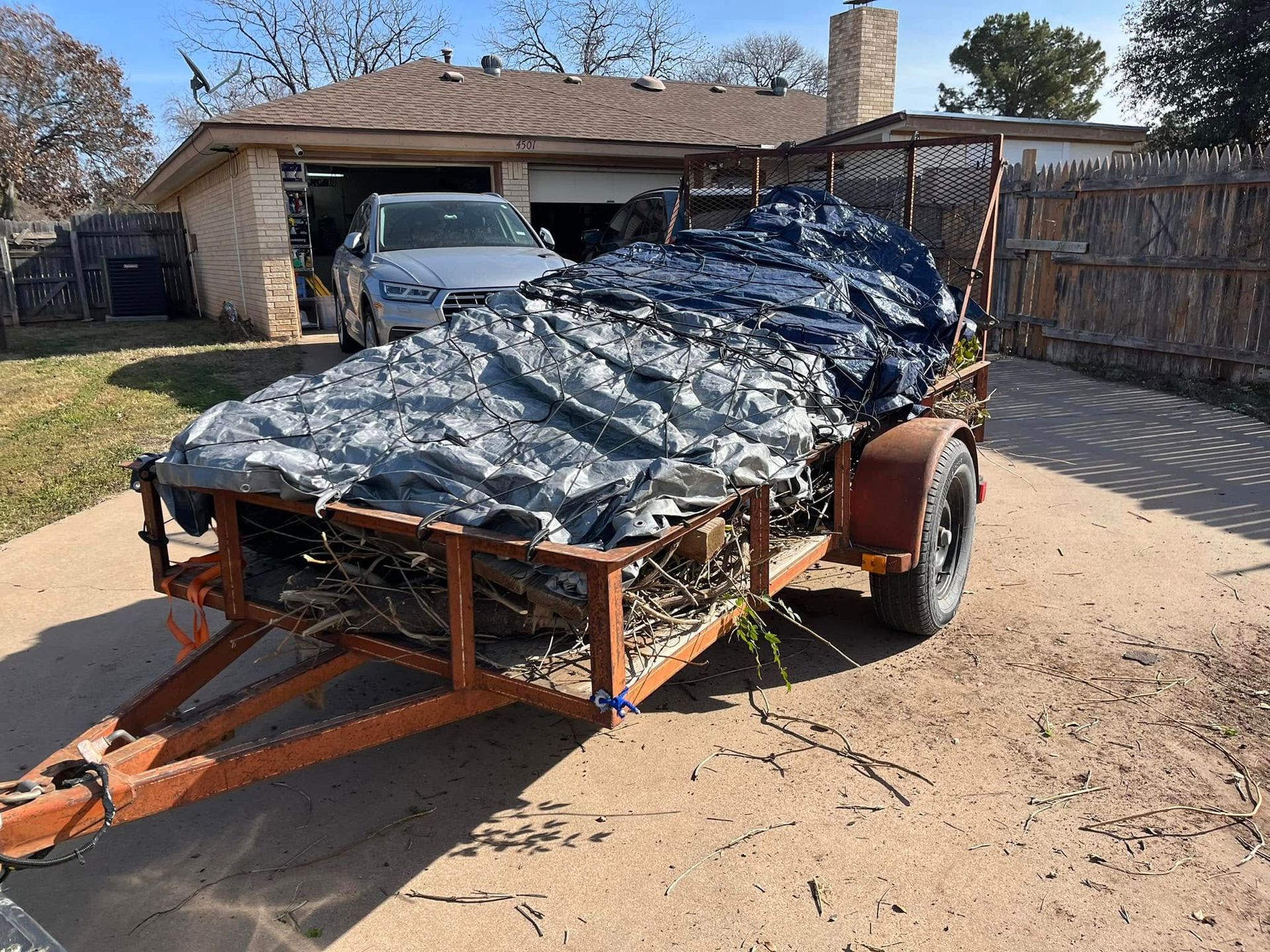 A trailer with a tarp on it is parked in front of a house.