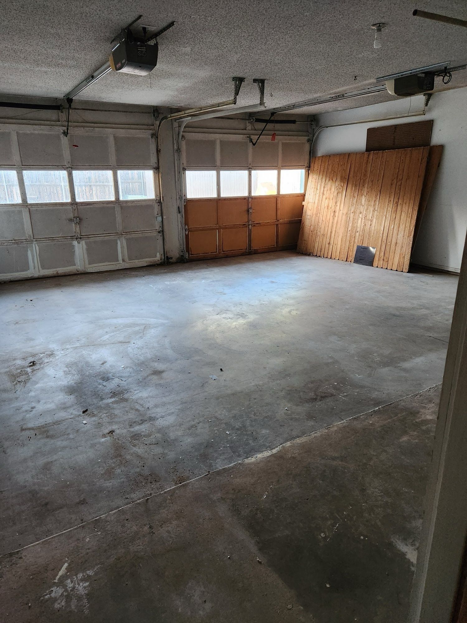 An empty garage with a garage door open and a wooden wall.