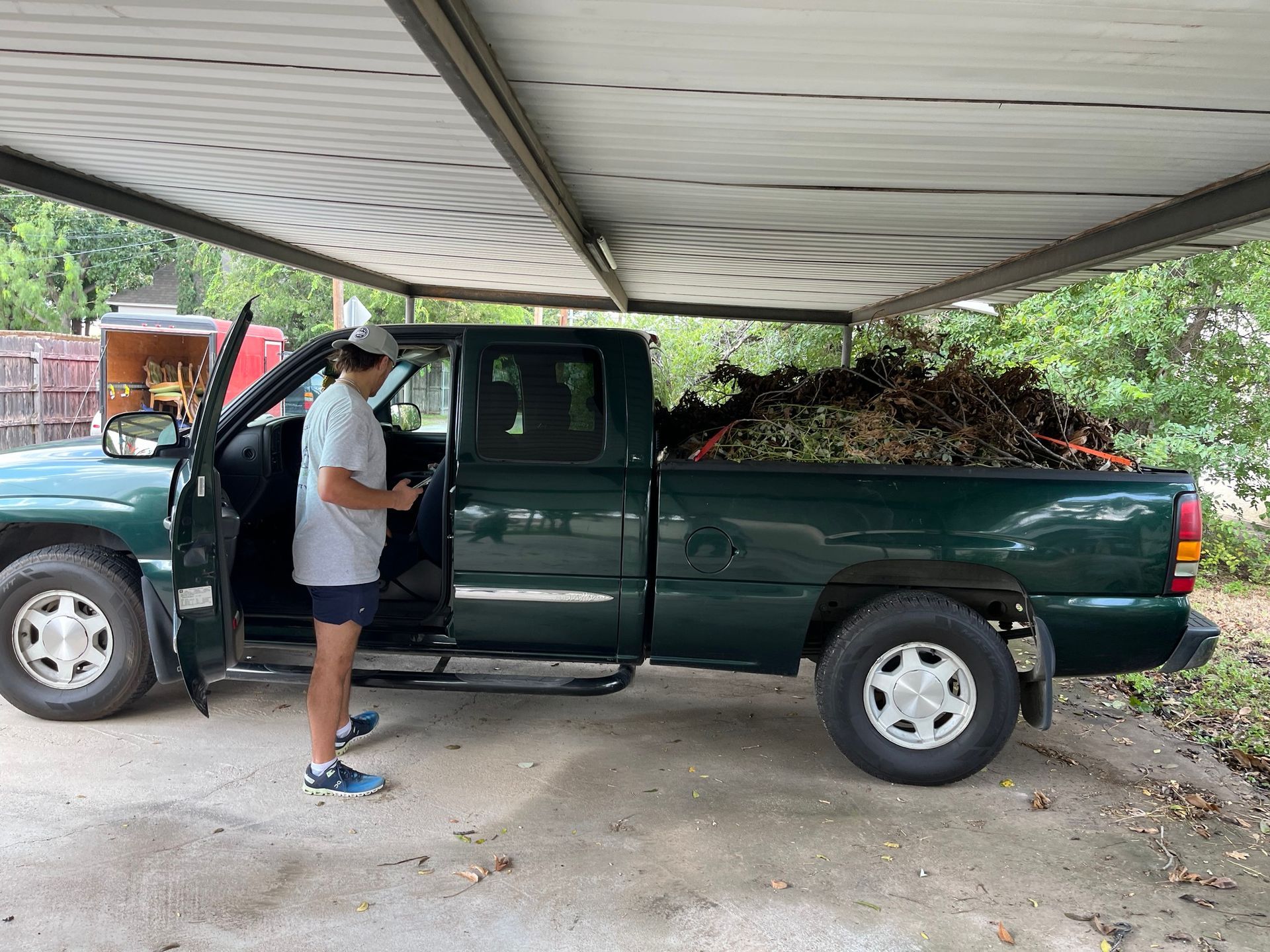 A man is standing next to a green truck under a shed.