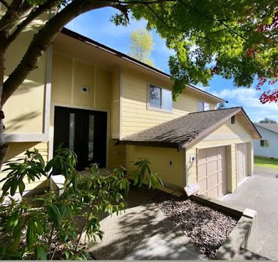 A yellow house with two garages and a tree in front of it