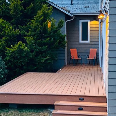 A wooden deck with two chairs on it in front of a house.