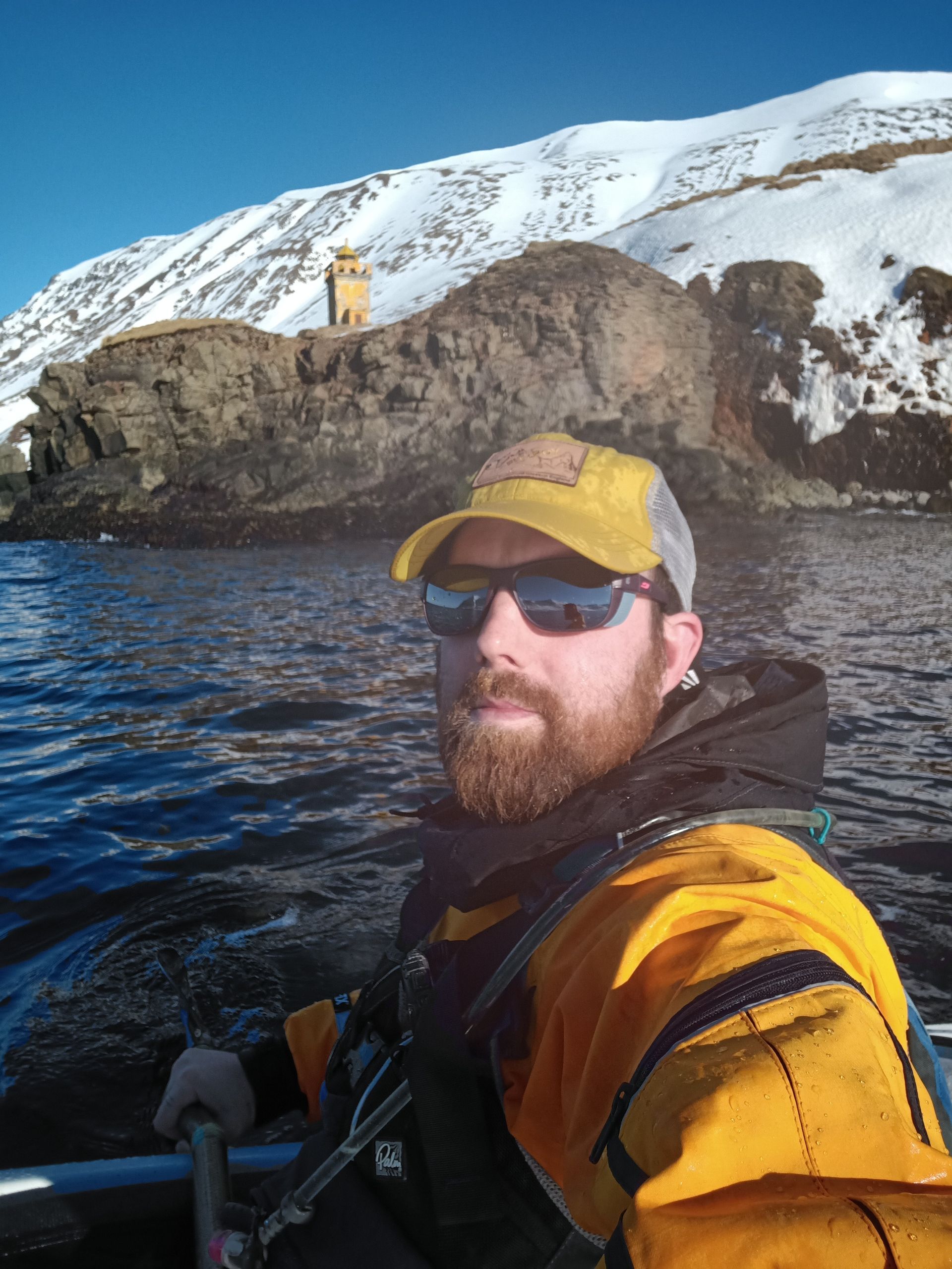 Bearded handsome man kayaking with yellow lighthouse and snow on the mountains.