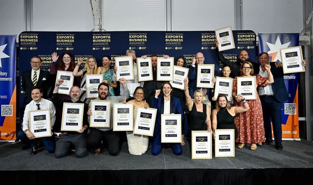 Group of people on a stage holding framed awards in front of a blue backdrop with logos