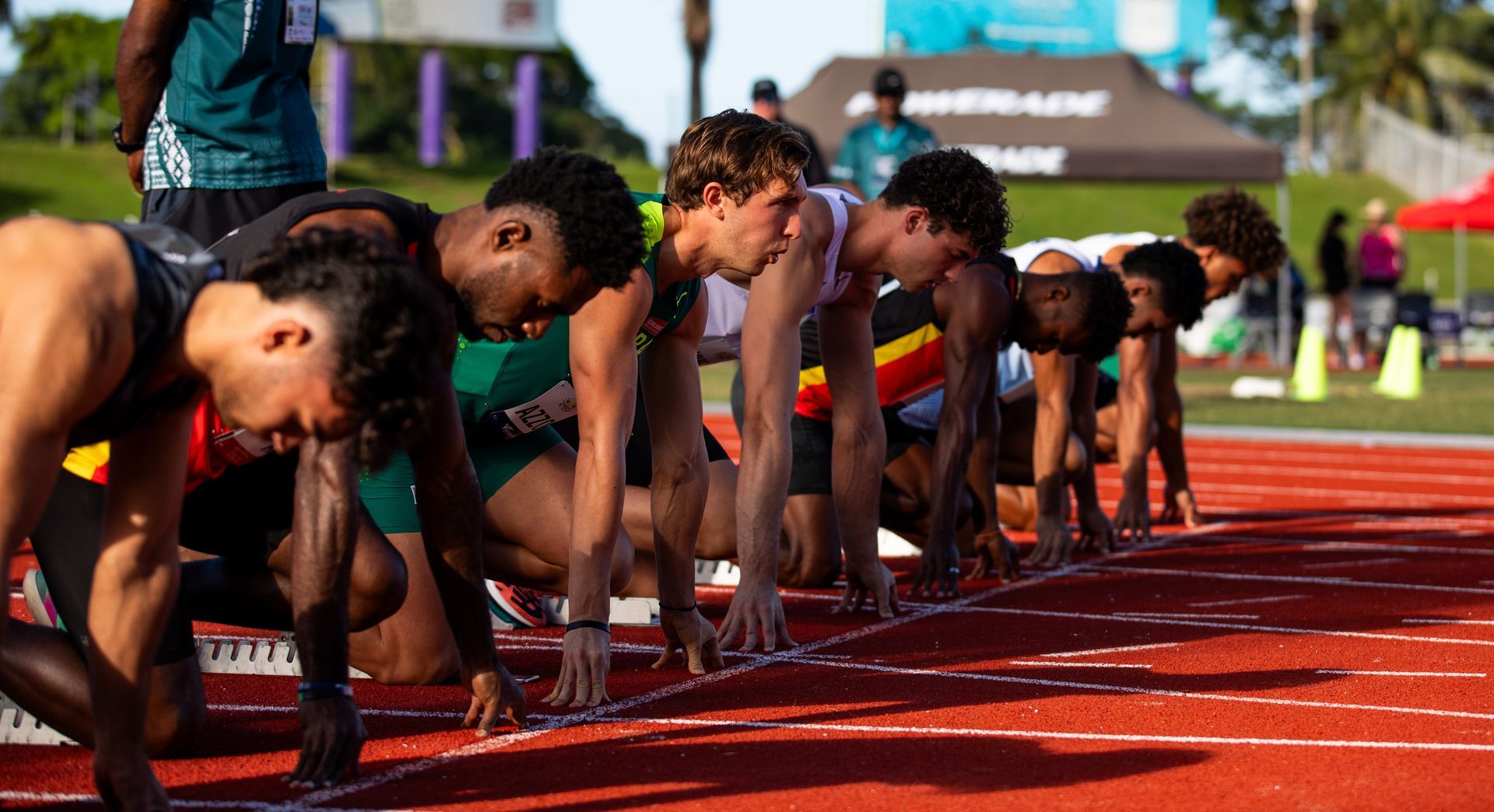 Sprinters crouched at the starting line on a red track, ready to race under bright daylight