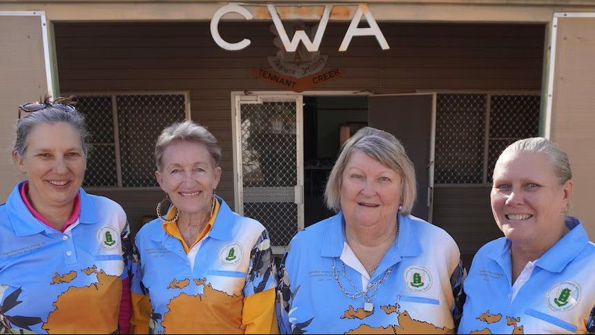 Four people in white and orange shirts standing outside a building with “CWA” above the entrance