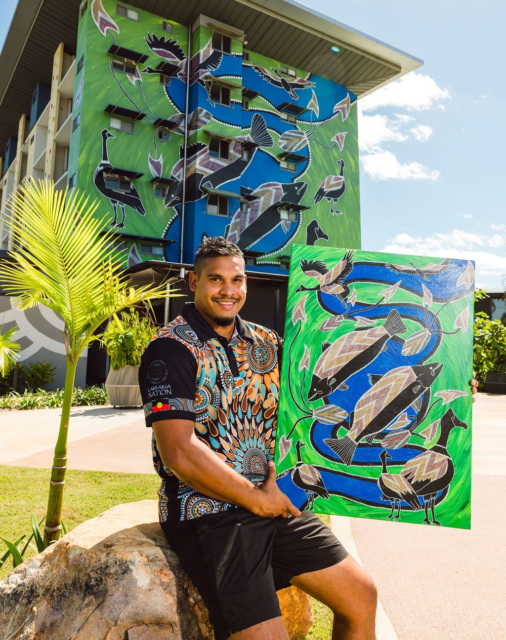 Man holding a green and blue abstract sculpture outdoors in front of a modern building