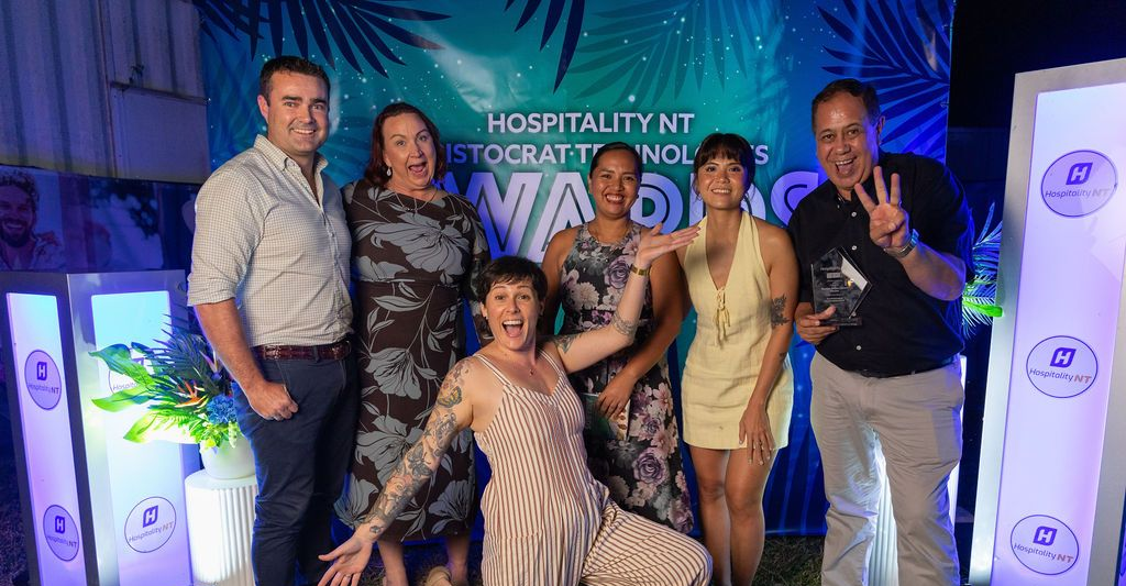 Group posing at a lit event backdrop with glowing columns and blue-green lighting