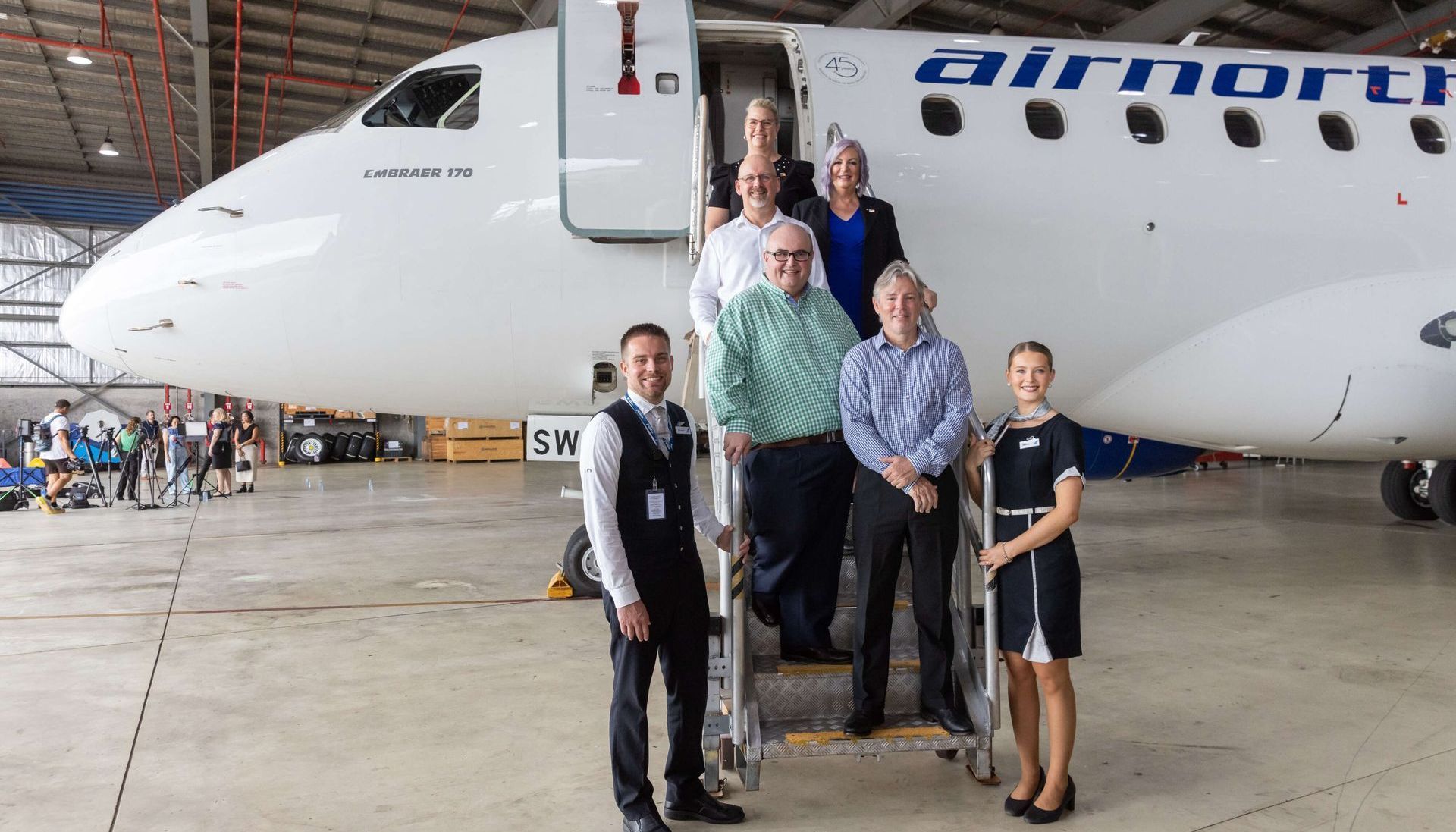 People posing on the steps of an Airnorth Embraer jet in a hangar.