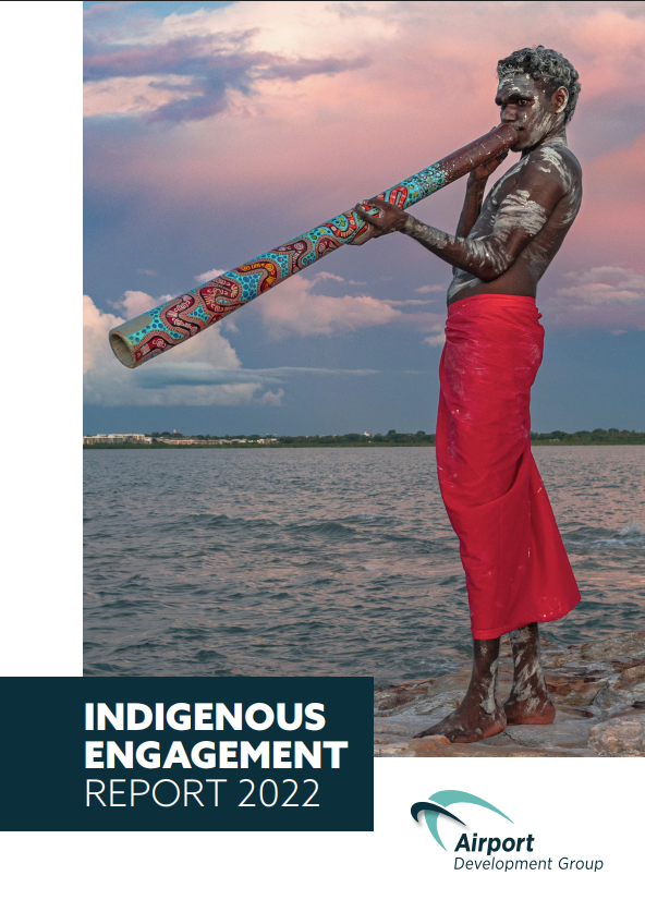 Aboriginal man playing a didgeridoo, wearing a red wrap, waterfront. Indigenous Engagement Report 2022 cover.