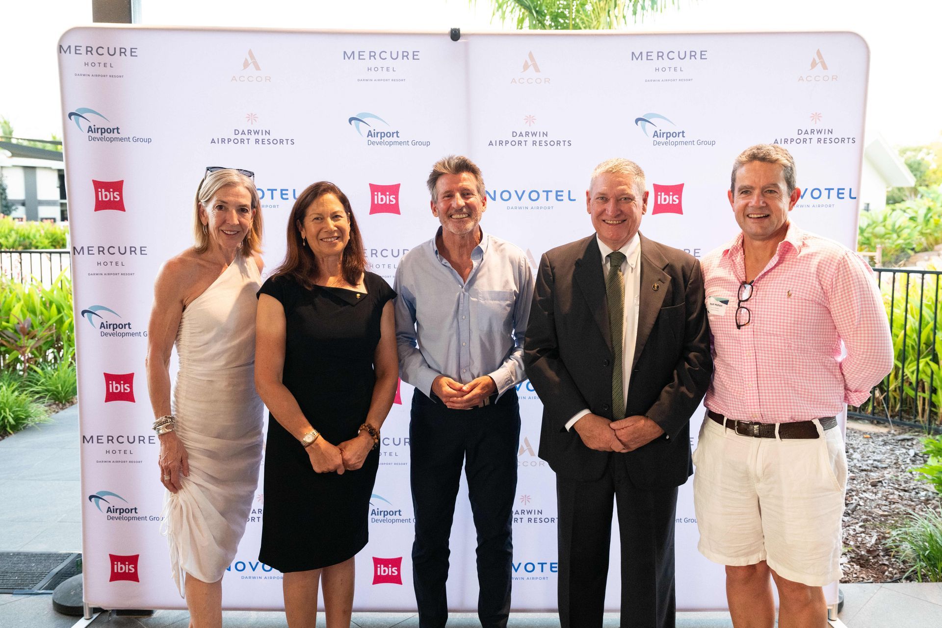 Five people posing in front of a sponsor backdrop at an outdoor event