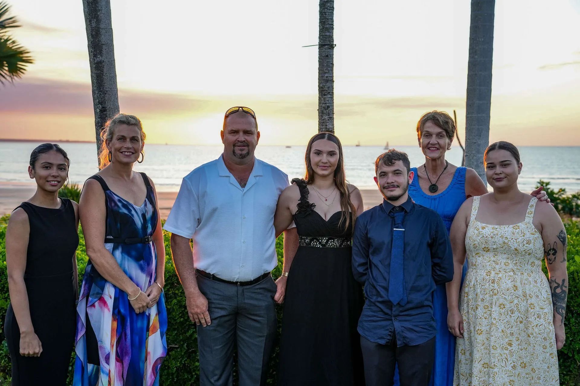 Group of people, diverse ages, posing together on a beach at sunset.