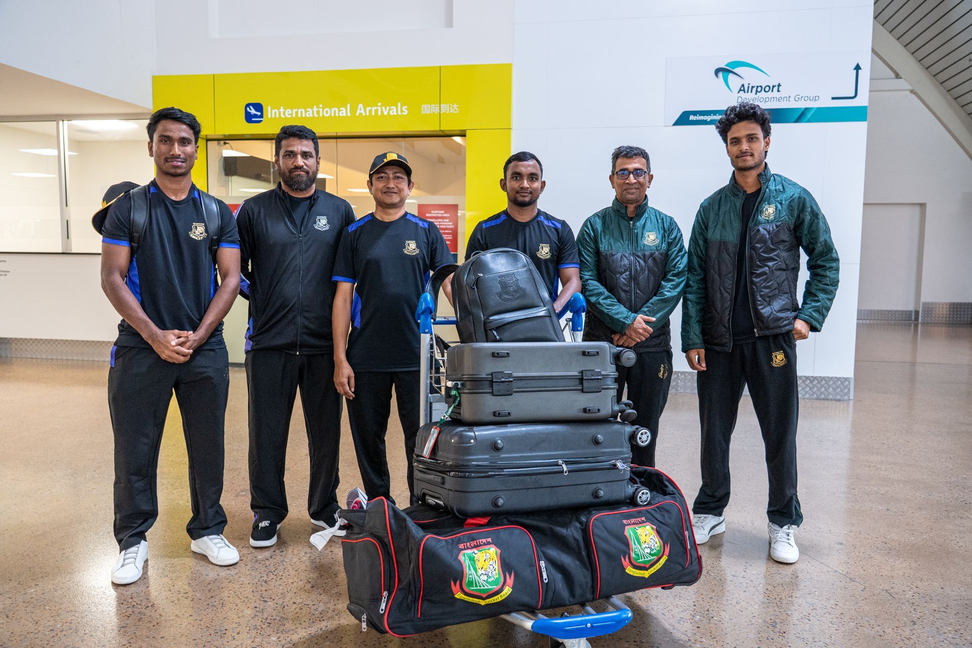 Six travelers standing at an airport with stacked luggage and duffel bags
