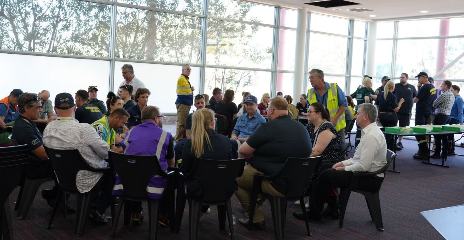 People in groups around tables in a bright room. Some are wearing uniforms.