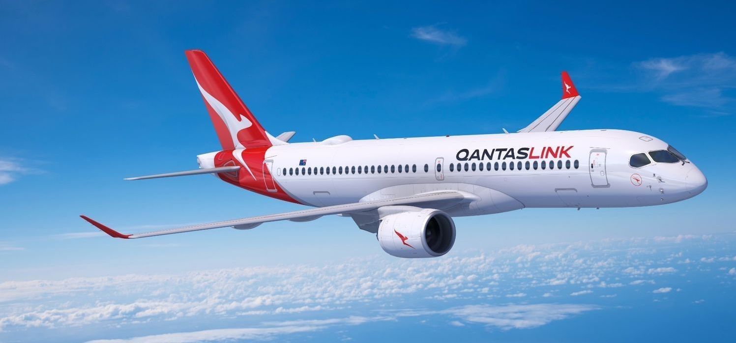 QantasLink airplane soaring in a bright blue sky with scattered clouds. White body with red tail and wing tips.