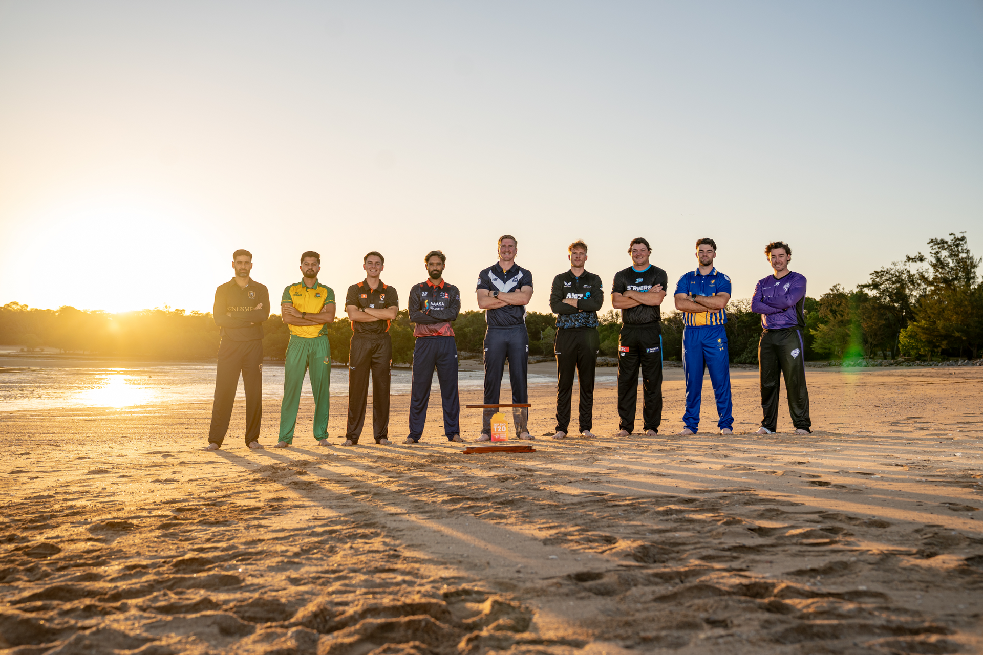 Nine people standing in a line on a sandy beach at sunset, with long shadows and a bright sky.