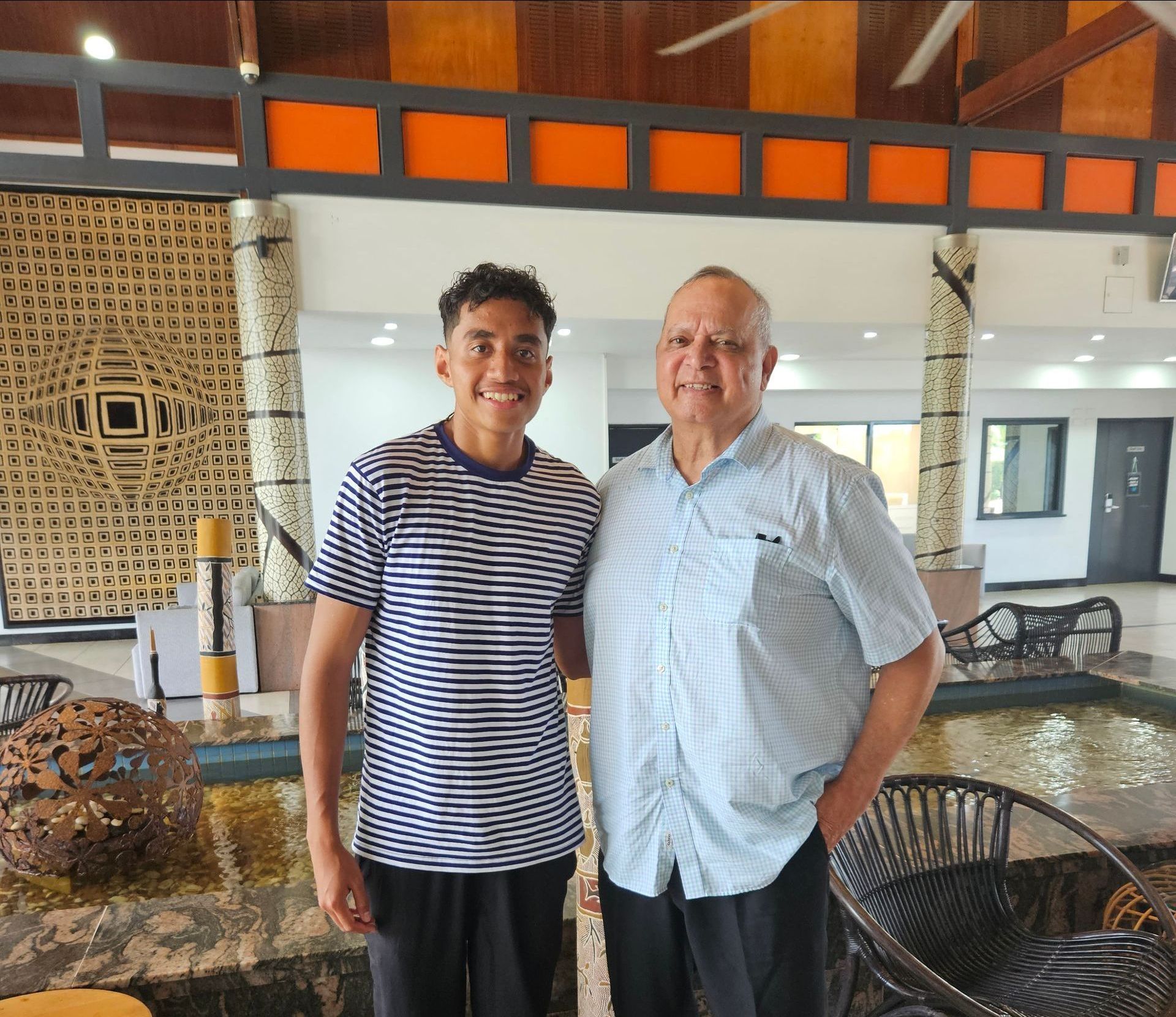 Two men smiling, posing together. One in striped shirt, the other in blue shirt. 