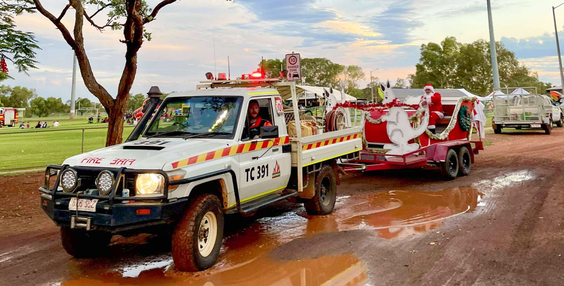 Decorated rescue vehicles parked on a muddy road, with people standing nearby under a cloudy sky.