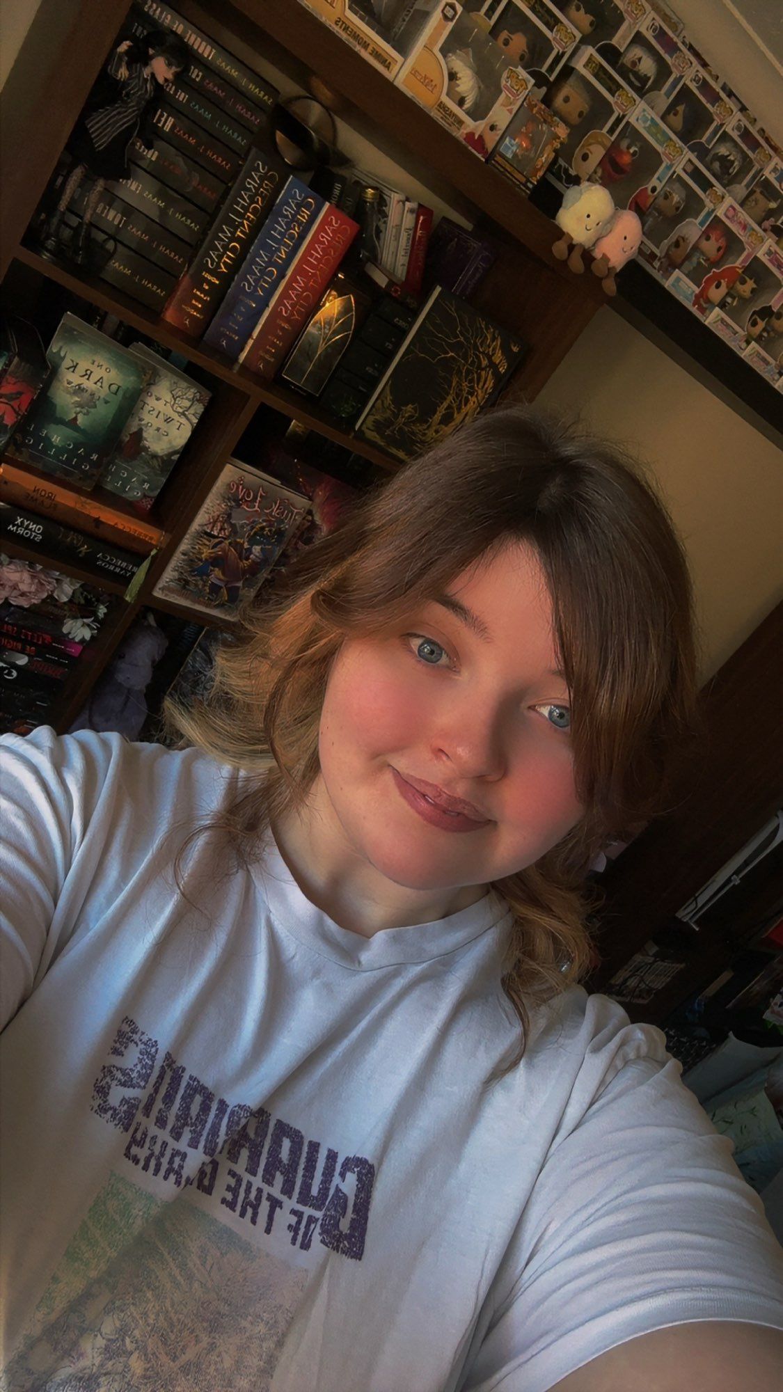 Woman in white shirt smiling at the camera, with a bookcase in the background.