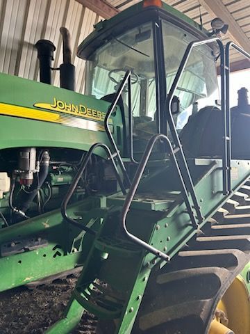 Close-up of the green entry steps and handrails leading into the cab of a parked John Deere tractor.