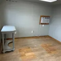 A light gray wall with a small table on the left and a window air conditioning unit mounted on the right.
