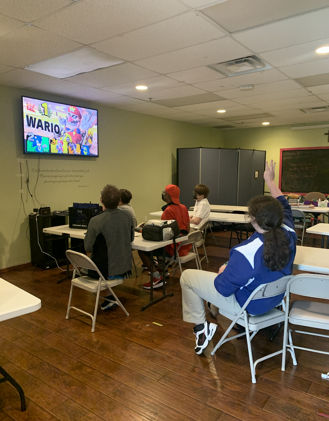 A group of students sits in a room watching a screen displaying 