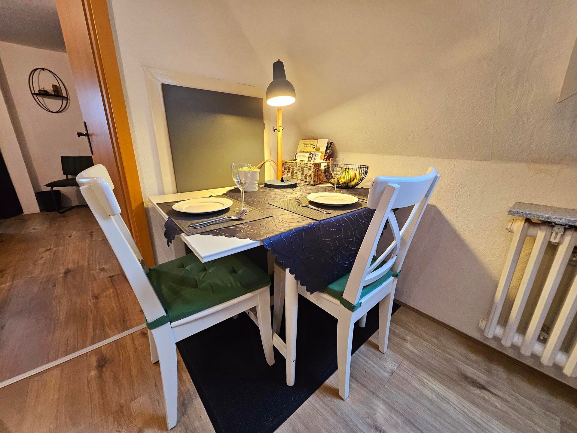 Eettafel gedekt voor twee in een knusse kamer, met wijnglazen, borden en een brandende hanglamp.