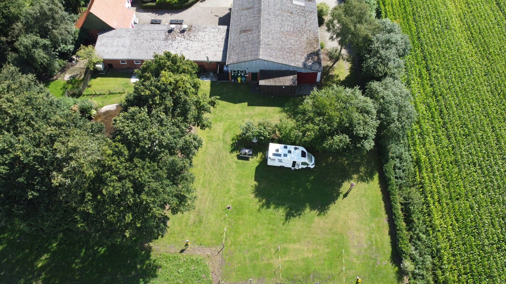 Luchtfoto van een huis en achtertuin met een witte tafel op het gazon naast dichte groene velden.