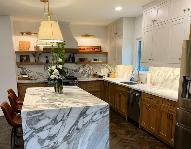 A luxury kitchen with a marble island, wooden cabinets, and white backsplash.