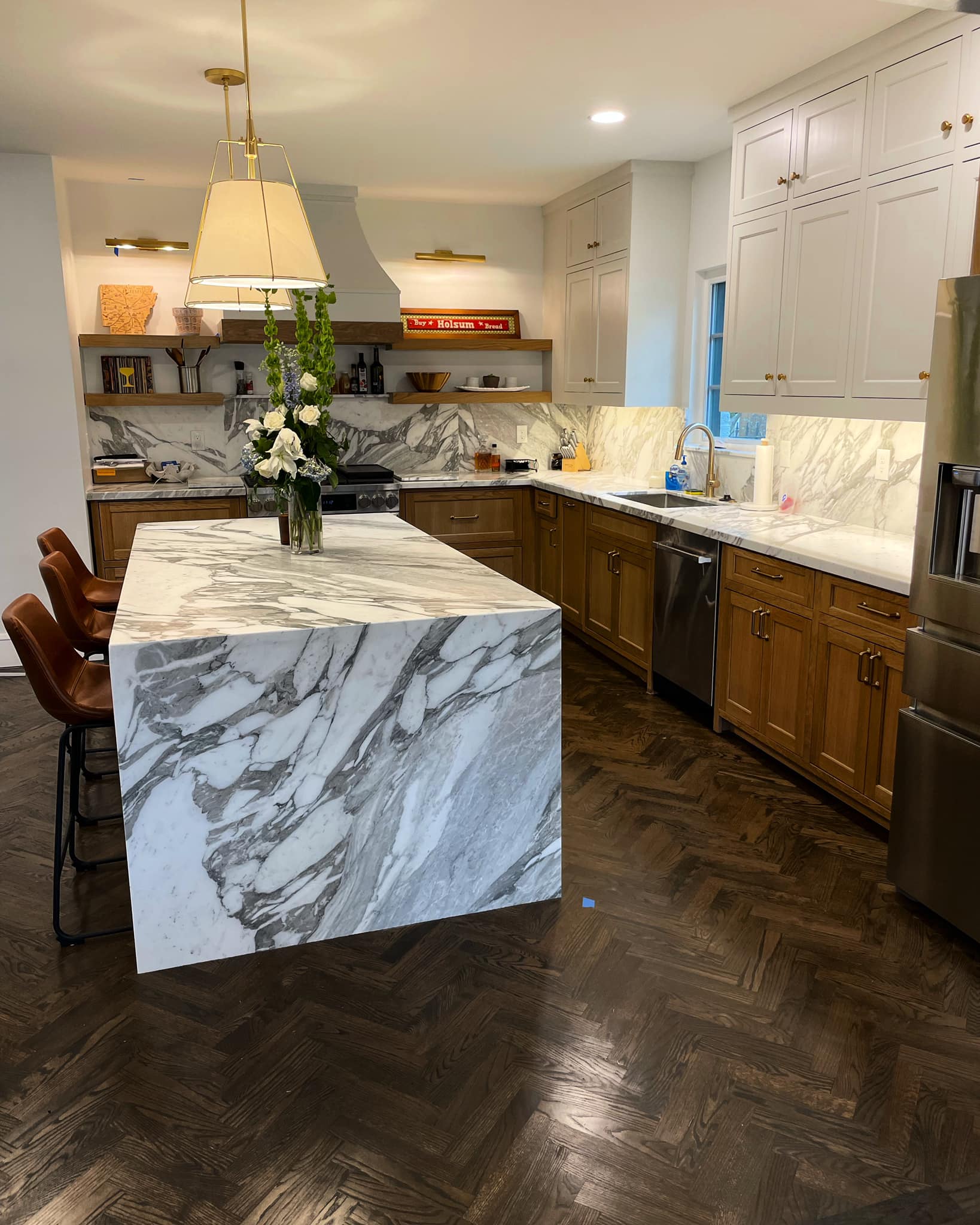 Spacious kitchen with a marble island, wooden cabinets, and dark herringbone floors.