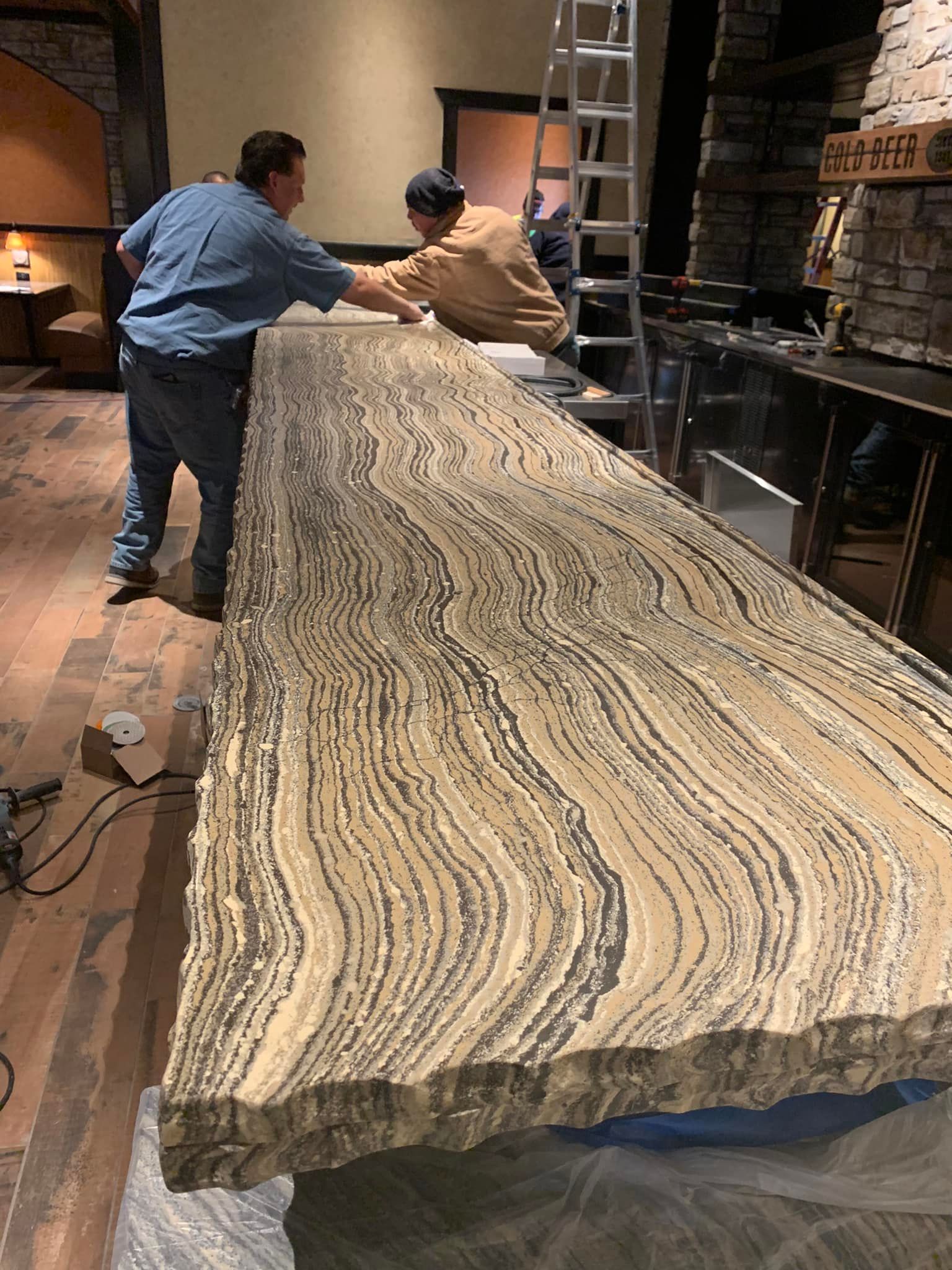 Two people working on a large, textured bar countertop. Interior shot, stone wall in background.