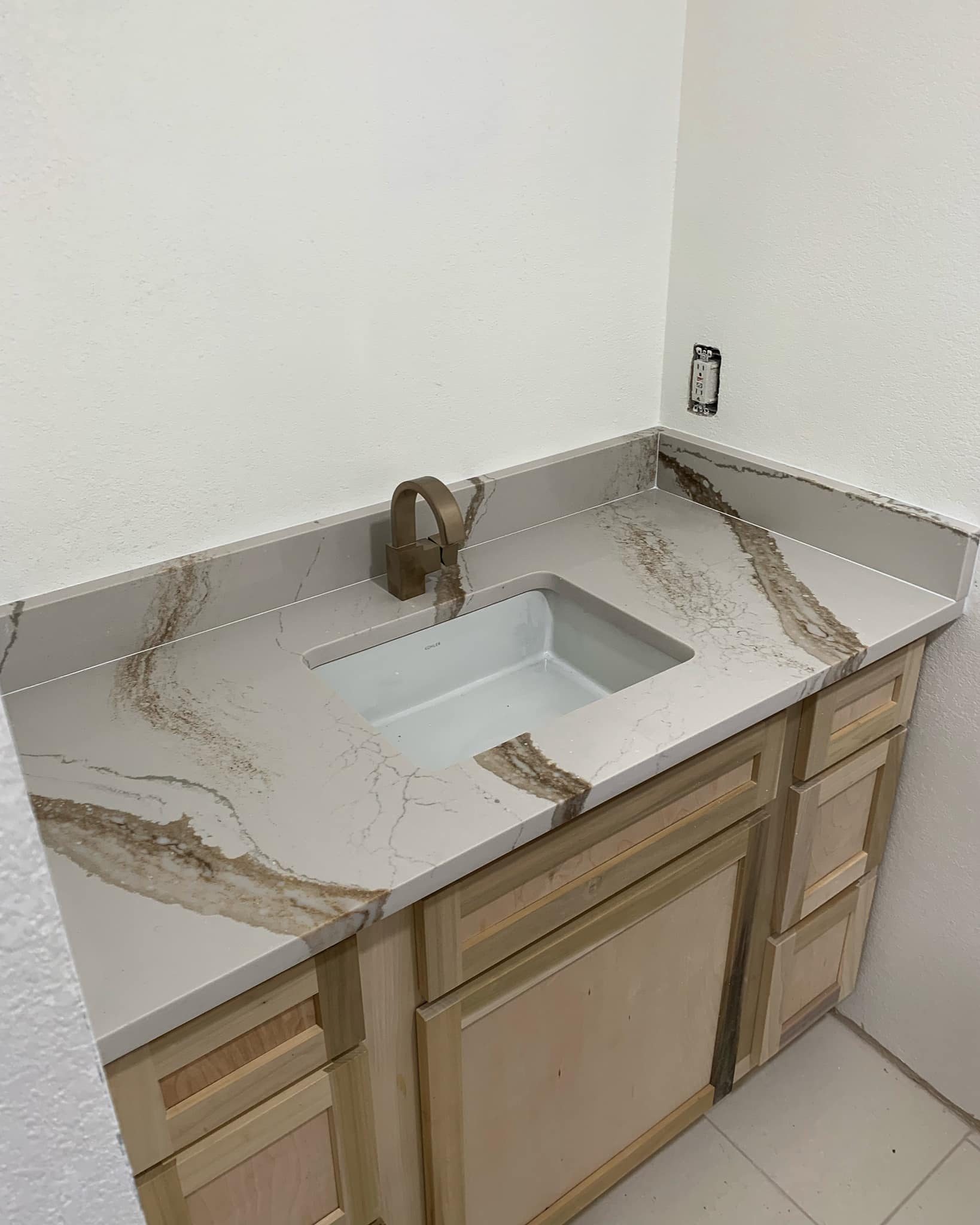 Bathroom vanity with a light wood cabinet, white sink, and light countertop with brown veining.