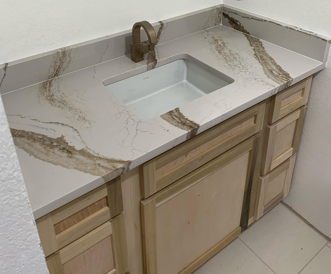 Bathroom vanity with light wood cabinets, white sink, and stone countertop with brown veining.