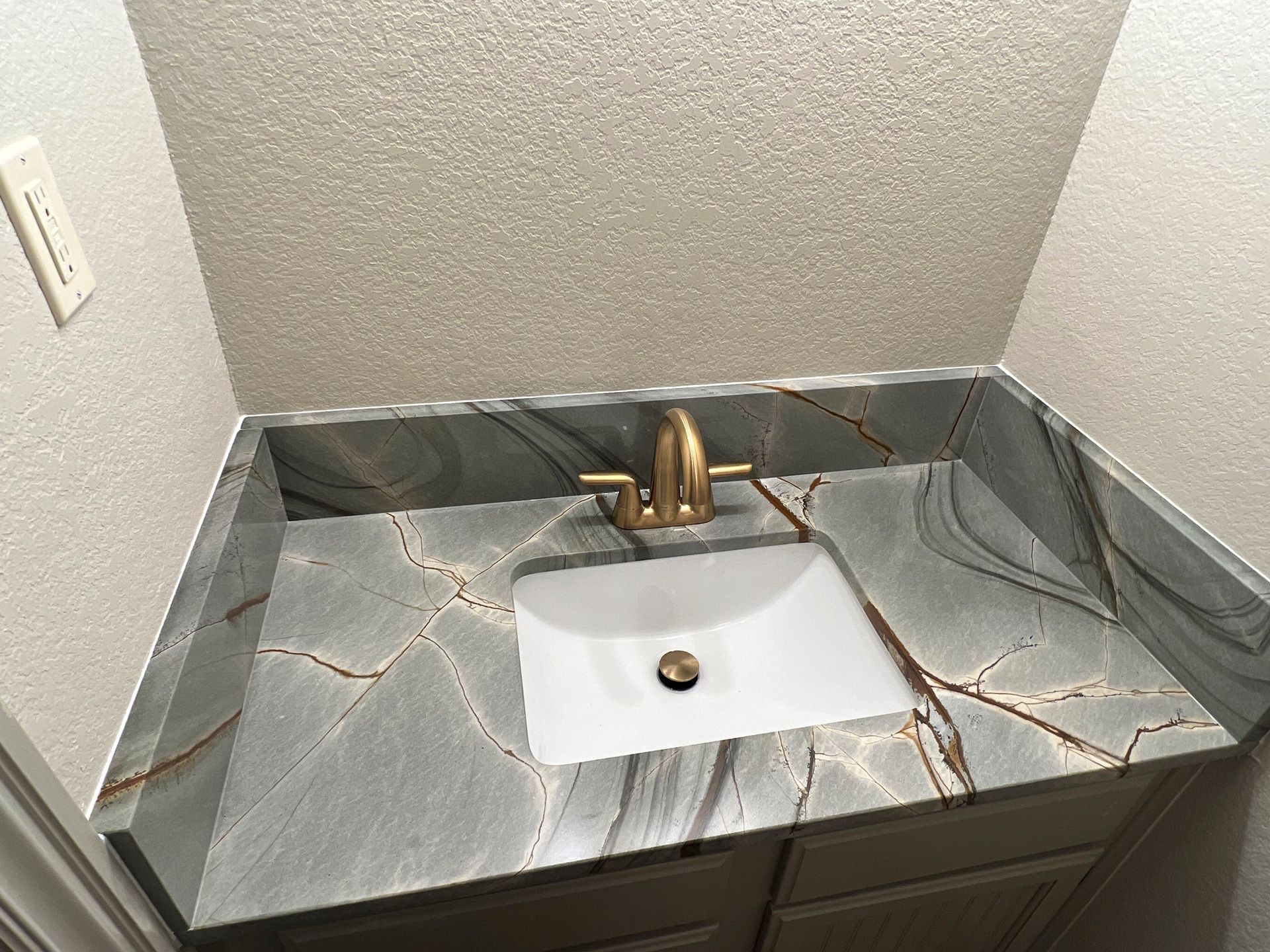 Vanity with gray and gold countertop, white sink, and gold faucet.