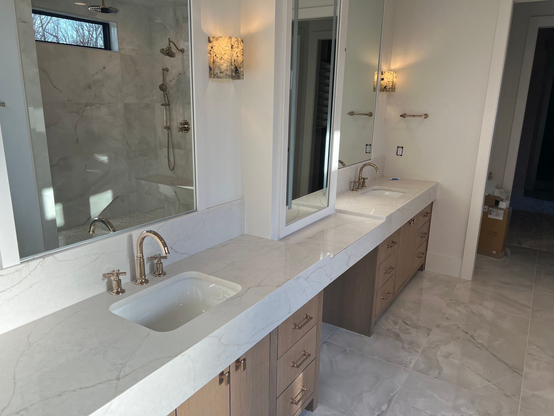 Bathroom with marble countertop, double sinks, large mirrors, and gold fixtures.
