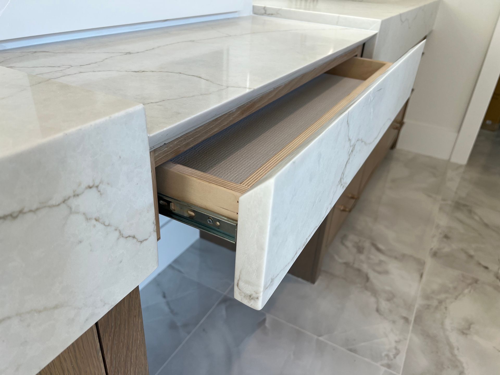 Open kitchen drawer under marble countertop. Drawer is partially extended.