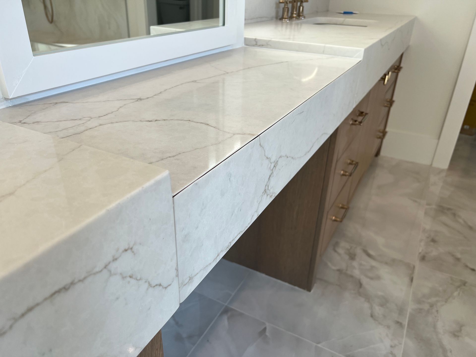 White marble countertop on light wood vanity with gold hardware.