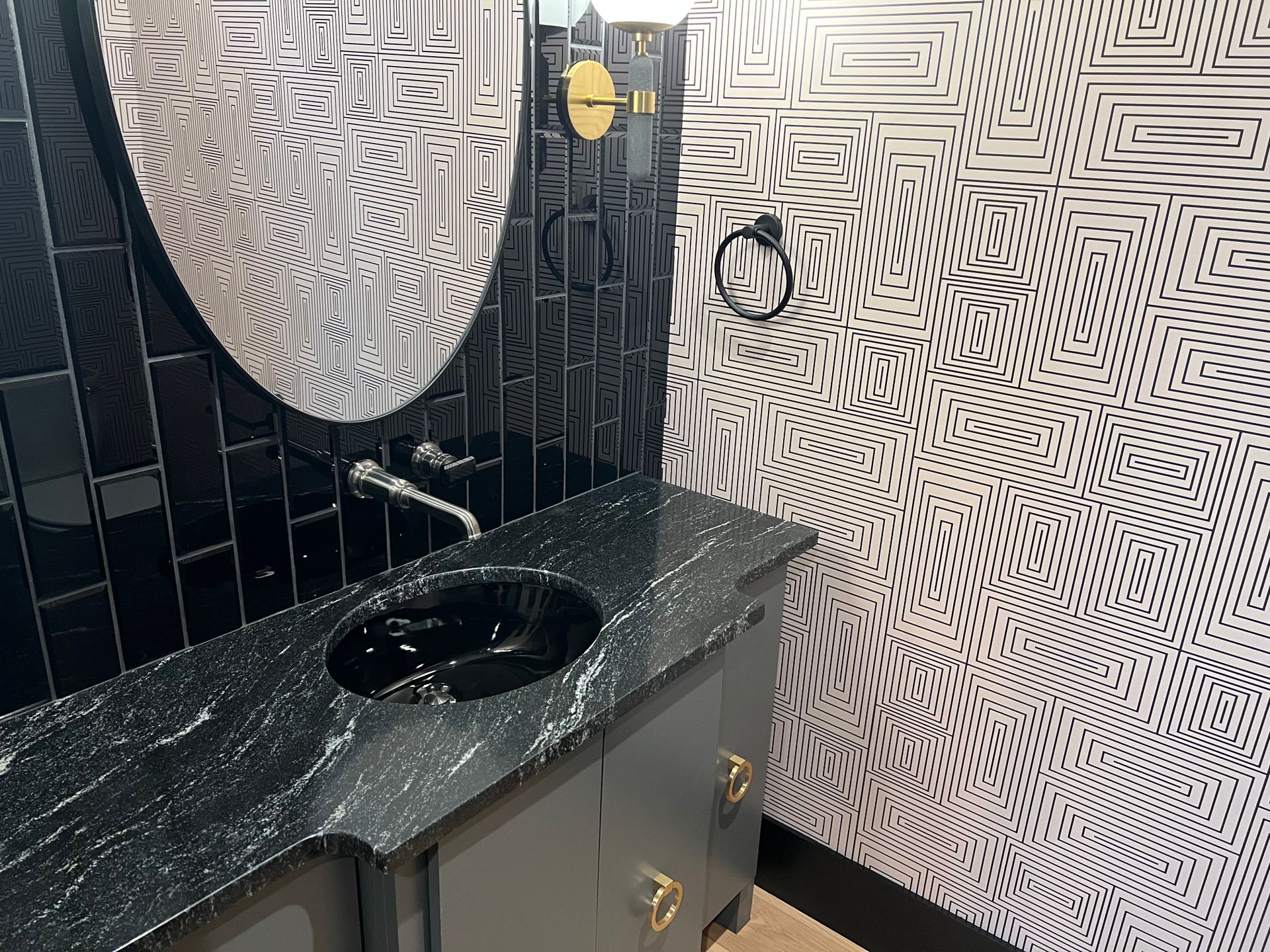 Bathroom with a black vanity, sink, and mirror. Black and white patterned wallpaper.