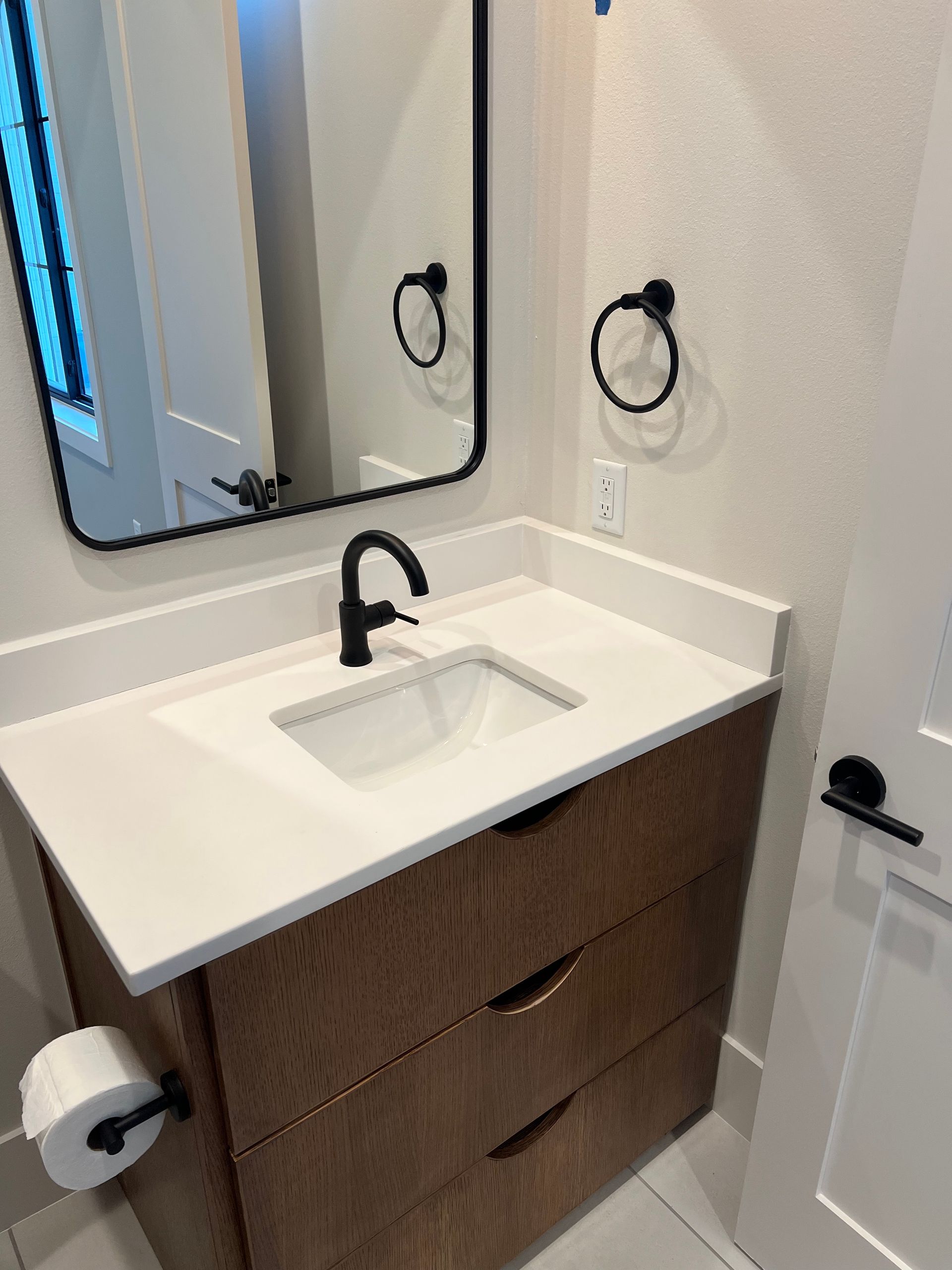 Bathroom vanity with a brown cabinet, white countertop, black faucet, and mirror.