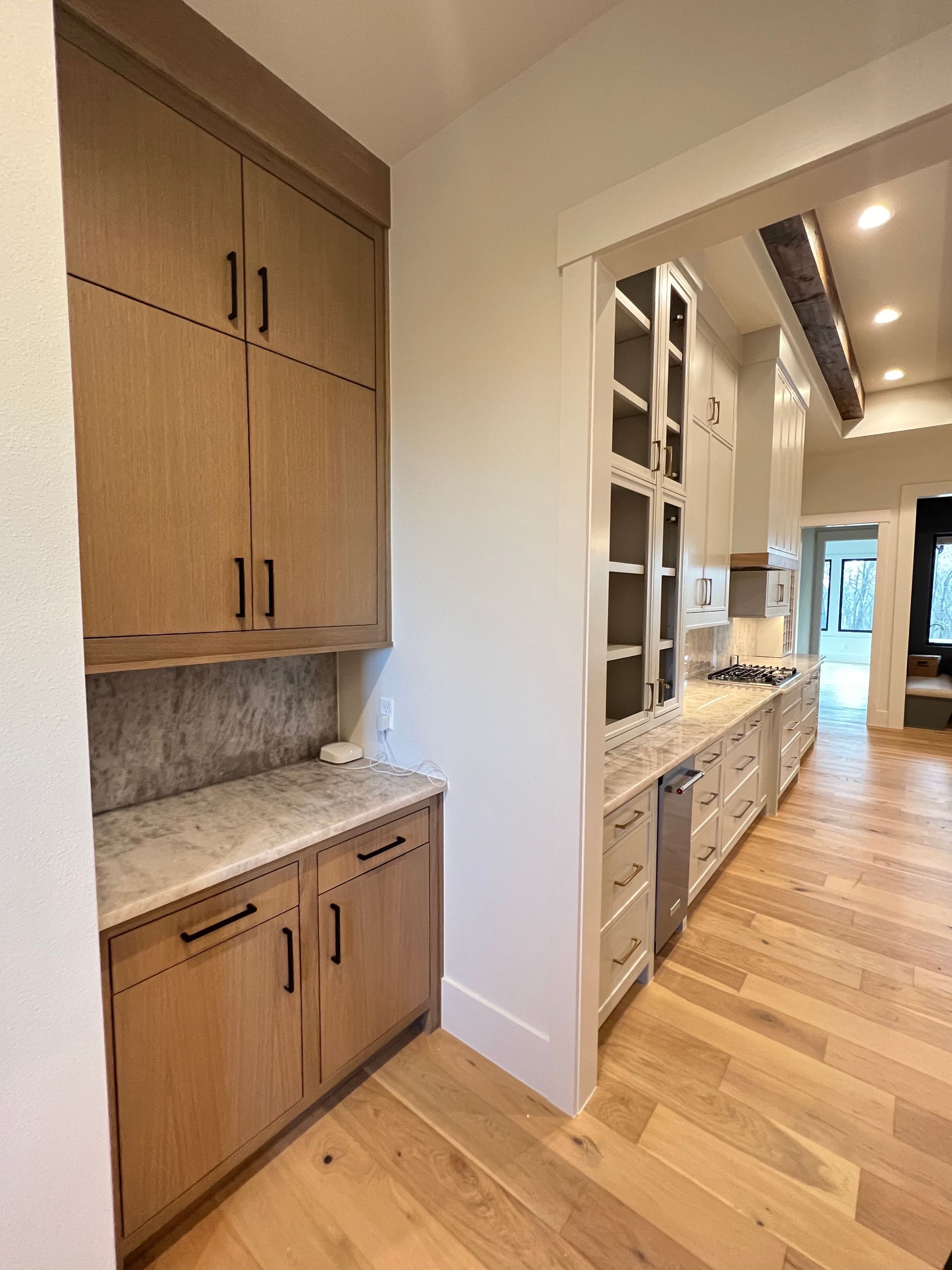 Oak cabinets with marble countertop in a kitchen. Light wood flooring and white walls.